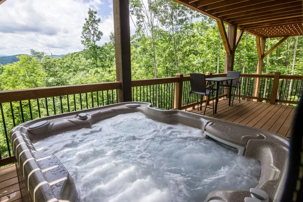 An exterior deck area featuring a bubbling hot tub, comfortable outdoor seating, and lush greenery all around. The atmosphere is tranquil and rejuvenating, offering a space for soaking and unwinding while enjoying scenic views—ideal for both relaxation and social gatherings.