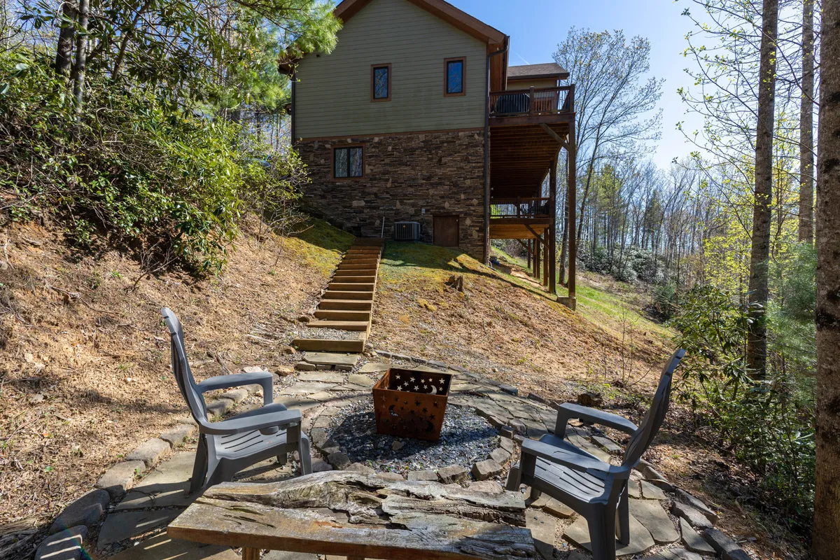 A warmly lit fire pit area with comfortable seating and steps leading up to the house, surrounded by nature. The scene invites family and friends to gather, roast marshmallows, or share stories under the stars.