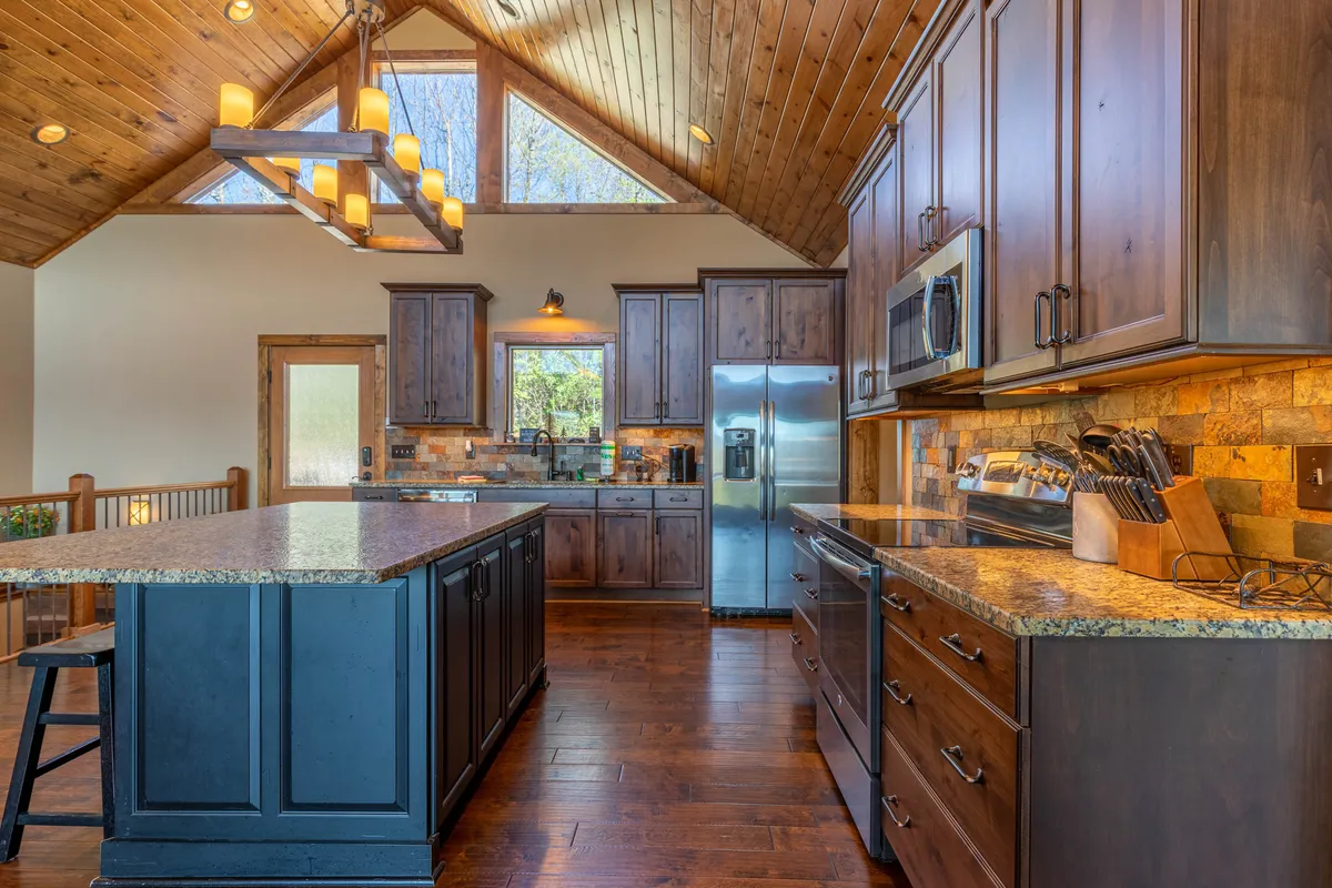 A bright, spacious kitchen with an island countertop, wooden cabinetry, modern stainless steel appliances, and large windows looking out onto the surrounding landscape. The space radiates warmth and sophistication, perfect for enjoying a morning coffee with a view.