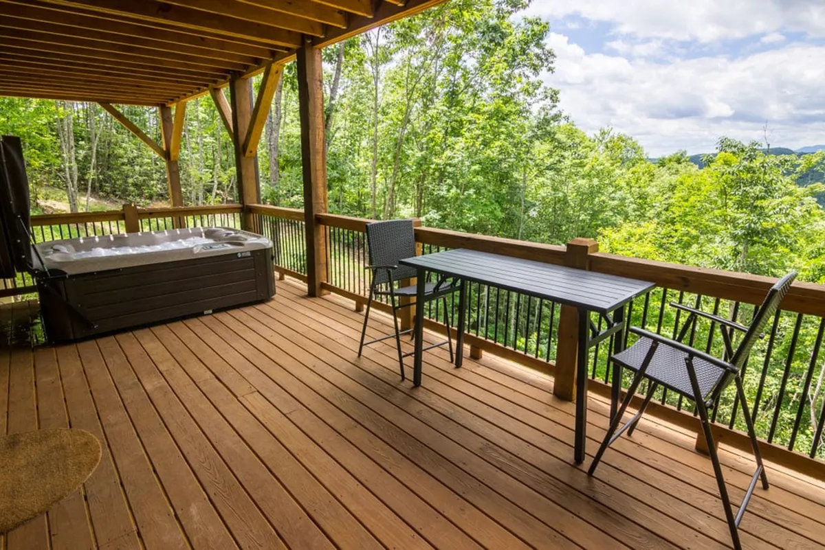 An inviting outdoor scene highlighting a hot tub, outdoor table and chairs, and lush greenery all around. The deck offers a comfortable space to relax, dine, or enjoy group gatherings in nature.