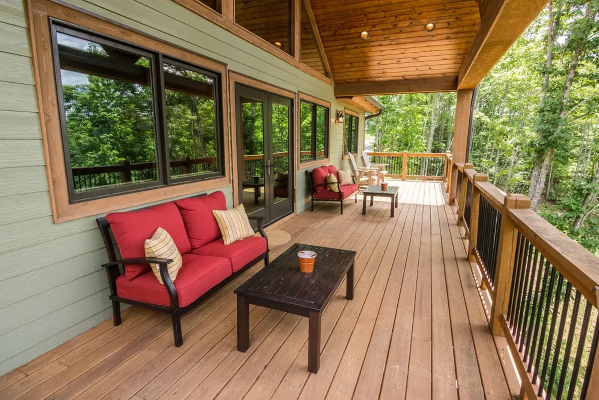 A wooden deck furnished with vibrant red sofas provides an inviting space to relax surrounded by green trees and mountain air. The expansive windows hint at panoramic scenic views, making this spot perfect for morning coffee, sunset watching, or stargazing under the clear mountain sky.