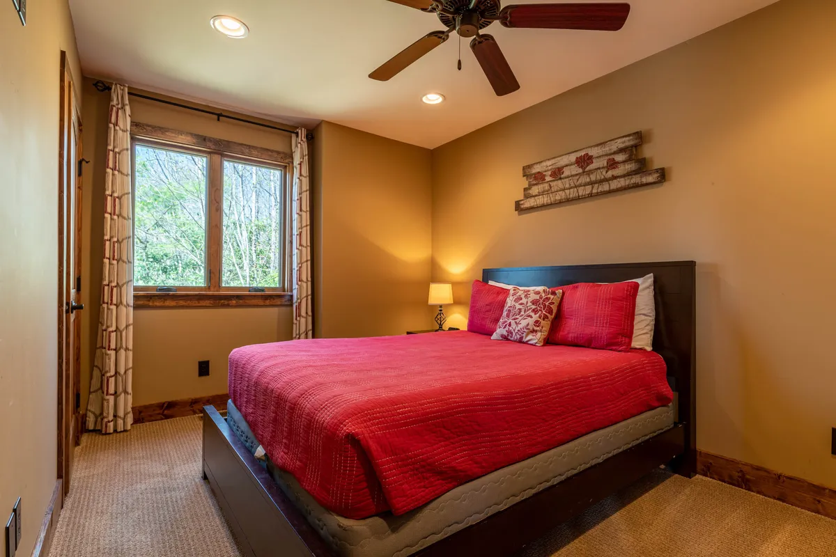 A cozy bedroom featuring a bed with a rich red blanket, a large window that lets in ample natural light, and decorative wall art. The space is designed for relaxation, with inviting textures and a comfortable atmosphere ideal for unwinding after a day outdoors.