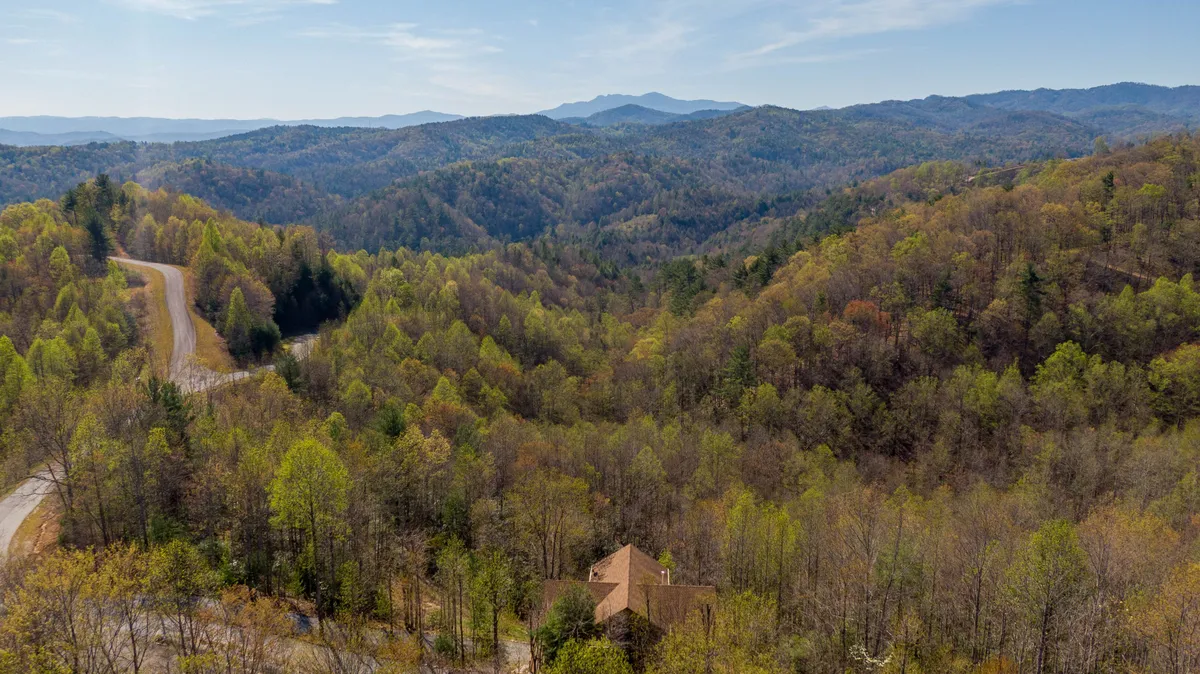 A sweeping view of a mountain range bordered by dense forest, with a winding road leading to a solitary house. The image is bathed in soft light, evoking a serene and private atmosphere, with nature’s grandeur front and center.
