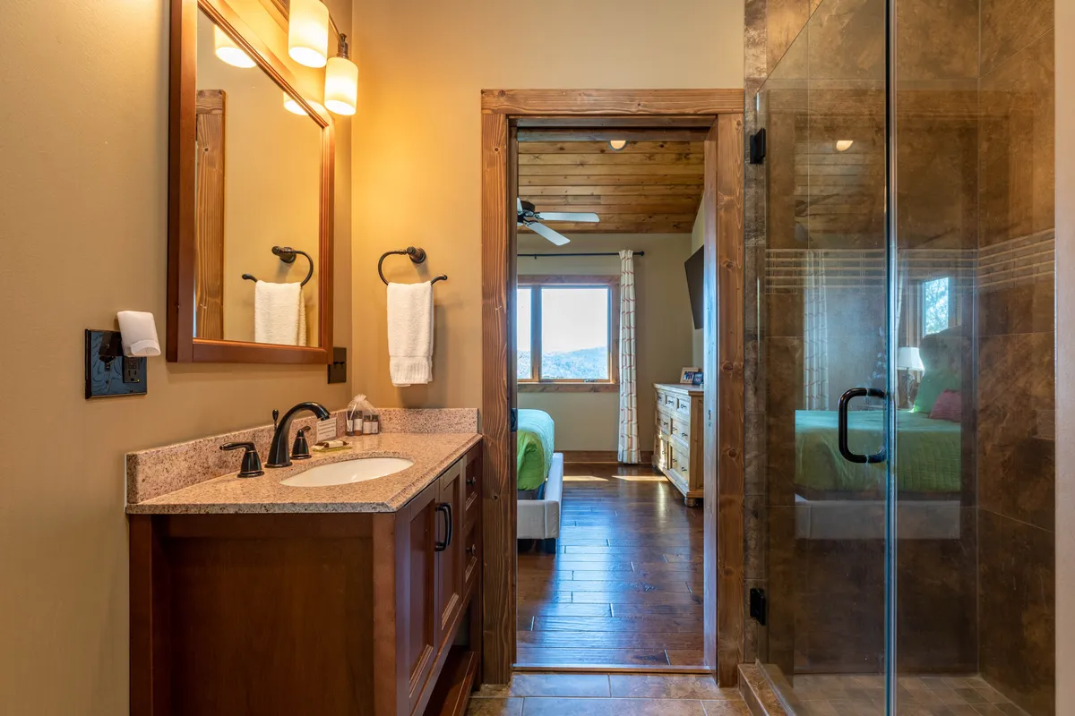 A bathroom with a contemporary vanity, sink, shower area, and a doorway leading towards a bedroom. The space is bright and inviting, suitable for morning routines or relaxing baths, and connects visually to the adjacent bedroom.