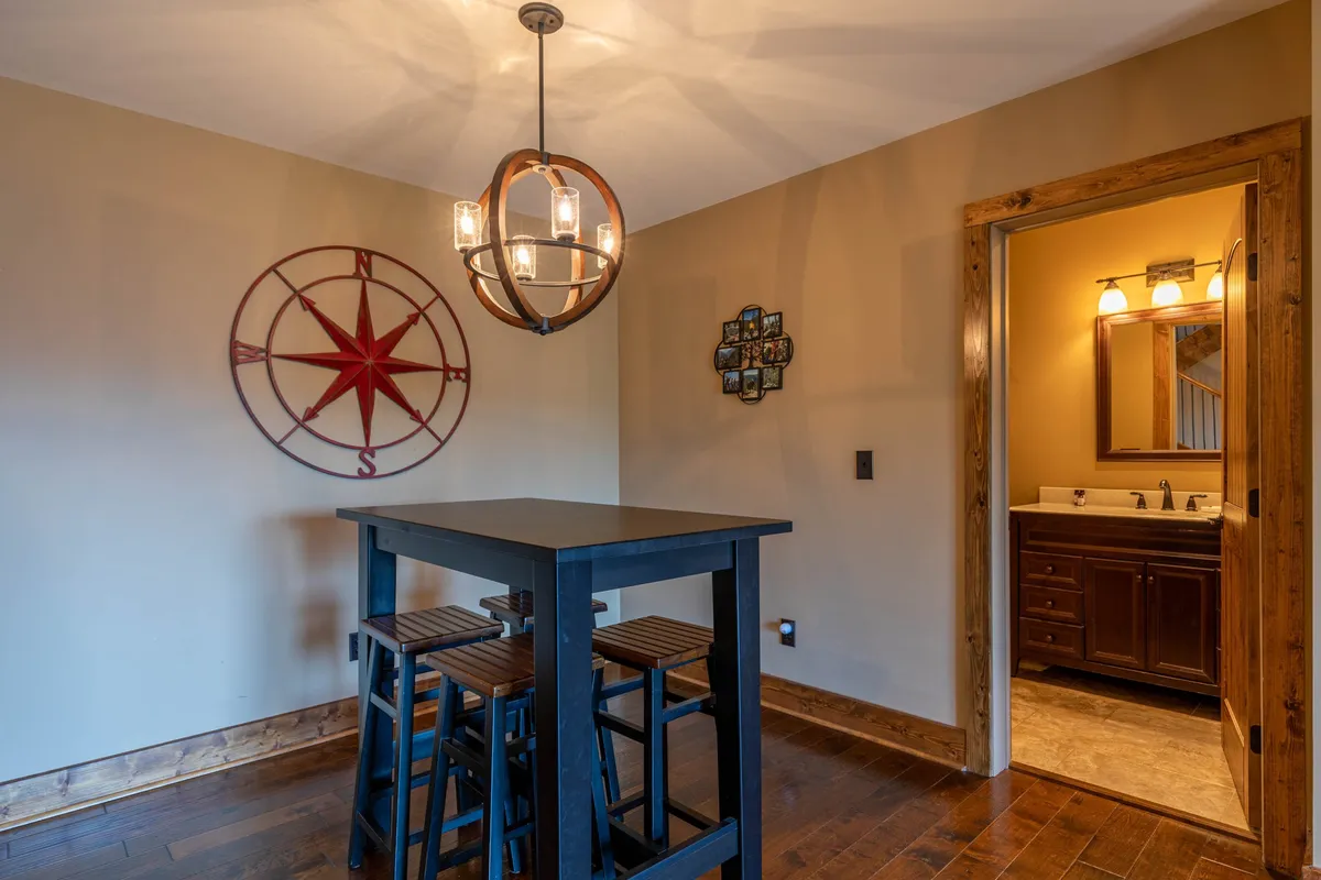 This inviting interior shot showcases a cozy café-style black table with stools, a hanging light fixture, compass wall art, and a bathroom entryway. The space suggests a setting for casual dining, board games, or coffee over conversation, promoting a communal and versatile area for relaxation and entertainment.