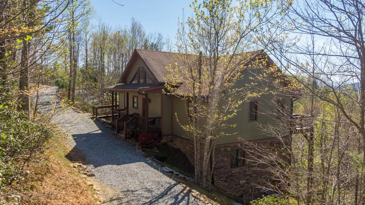 A wide exterior shot of the house with its gravel driveway surrounded by trees. This peaceful setting highlights the home’s private location within the community and its connection to the natural landscape.