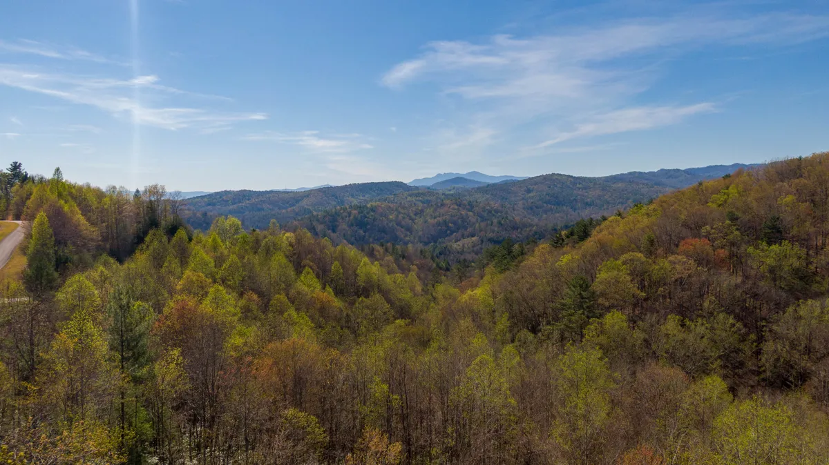This image captures a sweeping view of rolling hills covered in dense foliage with a majestic mountain range in the distance. The serene landscape invites exploration and hints at nearby trails and outdoor adventures, while the early sunlight suggests the promise of an exciting day in the High Country.
