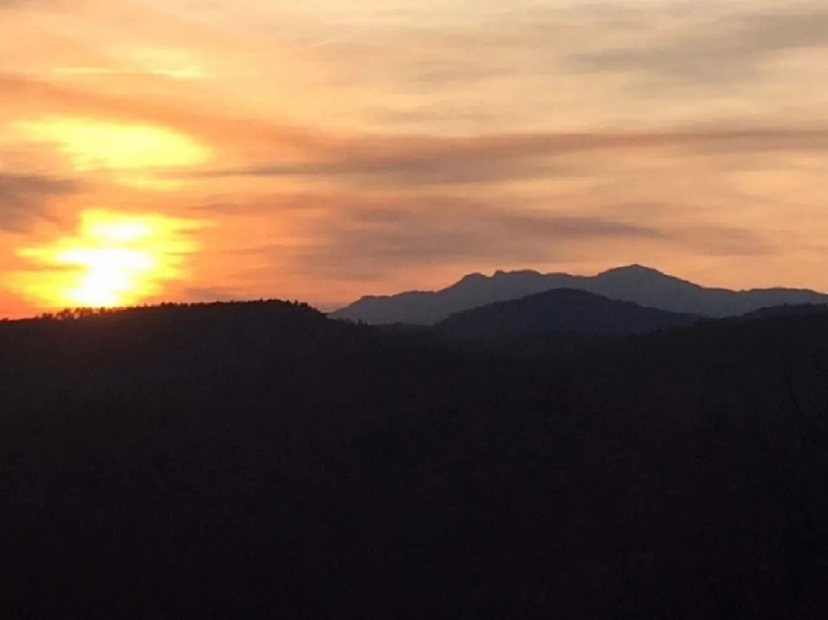 A sweeping view of a dramatic sunset over layered mountain silhouettes and dynamic clouds. The scene evokes the tranquility and awe of evenings spent outdoors, perfect for storytelling, s’mores around a firepit, or simply connecting with nature.